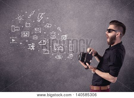 An elegant hipster guy trying to use a vintage camera with camera settings icons drawn on wall, like flash, white balace or ISO value concept