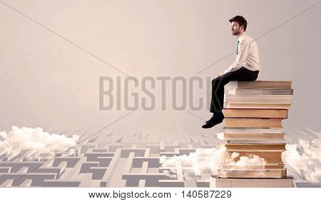 A serious businessman in suit sitting on a pile of giant books in front of a grey wall with clouds, labirynth