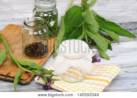 Alternative medicine preparing for filtering Comfrey ointment good for bones decorated with fresh comfrey and dried comfrey roots