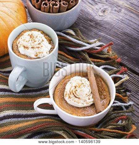 Quick meal breakfast snack in the microwave. Fragrant homemade pumpkin pie fall for five minutes in the cup portions with whipped cream and cinnamon on a wooden background. selective focus