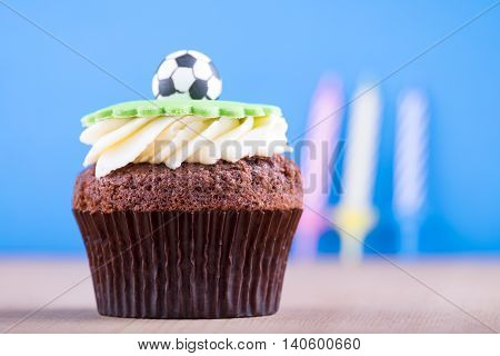 Delicious cupcake with ball icon on it and three colourful candles on wooden desk and blue background