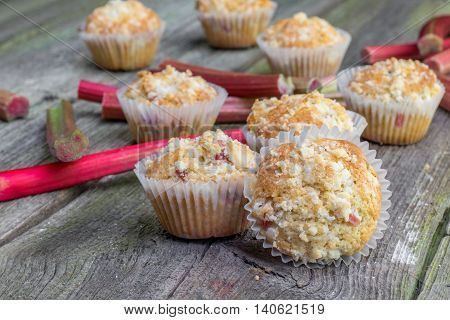 Rhubarb muffin with rhubarb petioles in the background on Old Wooden Board
