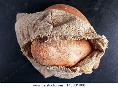 Freshly harvested organic sweet potatoes in a burlap bag on wooden table