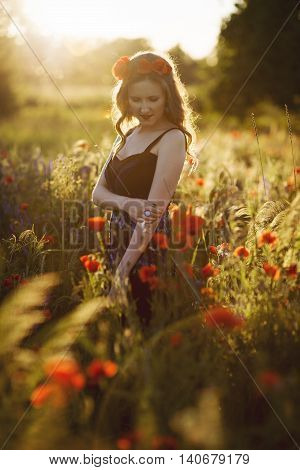 Beautiful young woman on the poppy field in sunlight