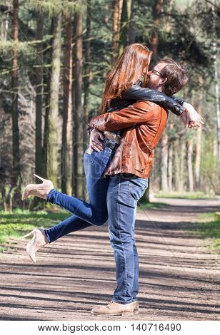 Young couple standing in spring park. Boy lift his girl and she bending her legs