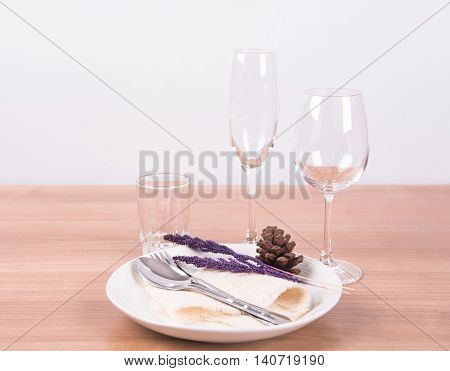 Dining table setting white plate with flower wineglass vintage crockery and spoon fork on wood table background.