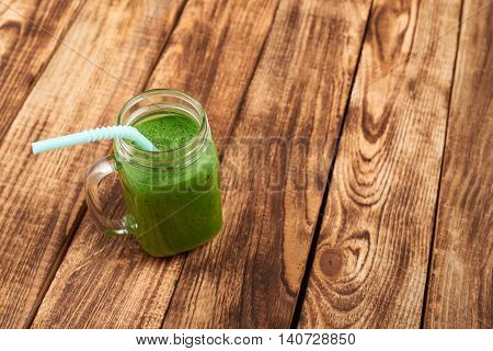 Jar tumbler mug with green smoothie drink over wooden background