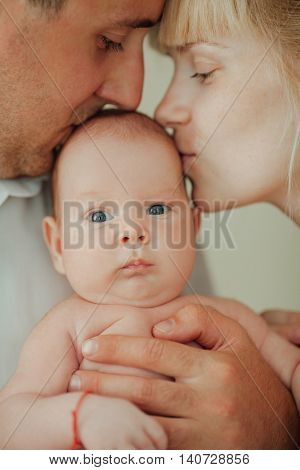 photo of happy mother and father kissing baby