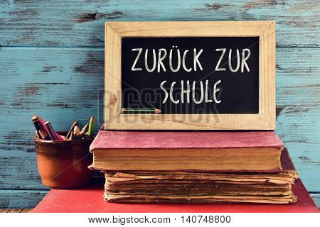closeup a chalkboard with the text zuruck zur schule, back to school written in German, on a pile of old books and a pot with some pencils, against a rustic blue wooden background