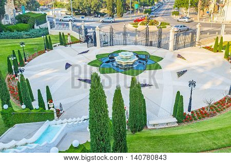 The scenic square decorated with the tiled pattern flower bed fountain in the middle surrounded by greenery and benches for visitors Haifa Israel.