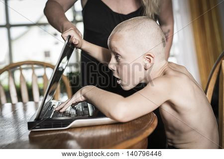 A boy with internet dependence playing with keyboard being dragged by mother from her computer