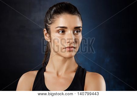 Portrait of young beautiful brunette  sportive girl posing over dark background. Copy space.