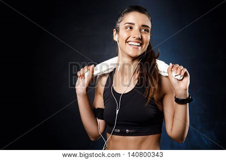 Young beautiful brunette sportive girl listening music over dark background. Copy space.
