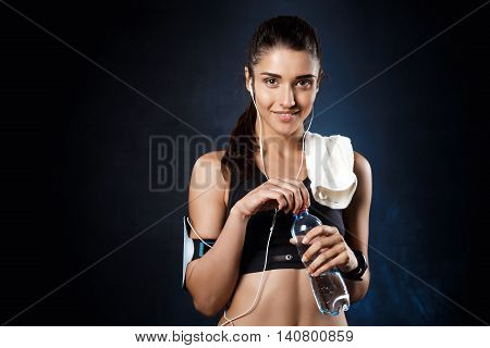 Young beautiful brunette sportive girl holding water over dark background. Copy space.
