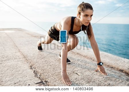 Young beautiful brunette sportive girl preparing to run over seaside. Copy space.