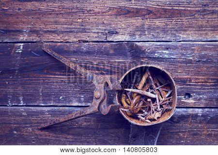old rusty pinchers with can of nails on wooden boards background