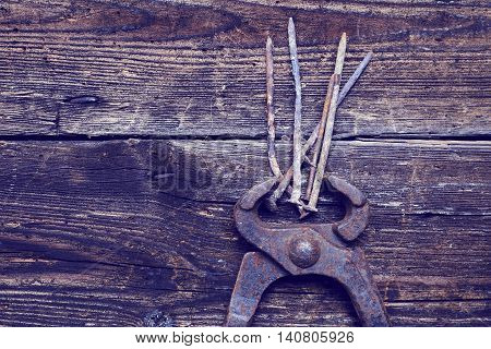 old rusty tongs with nails on wooden boards background