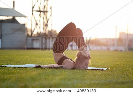 Young blonde woman in sportswear practicing yoga in park. Scorpion Pose Chest Stand Head to Foot.