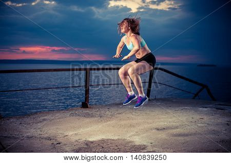 Fit woman in sportswear doing squat jumps. Fitness workout outdoors.