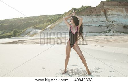 Sexy brunette Woman in black swimsuit with long black hair and red lips on the background of sands career