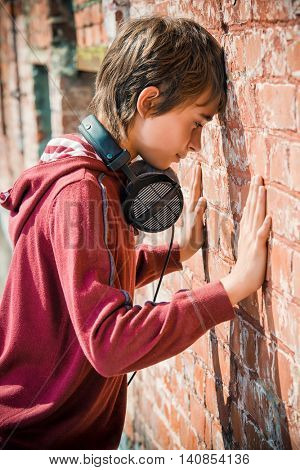 Teen boy standing in the street, turned away to face the wall. Sadness, depression. Teenage problems.