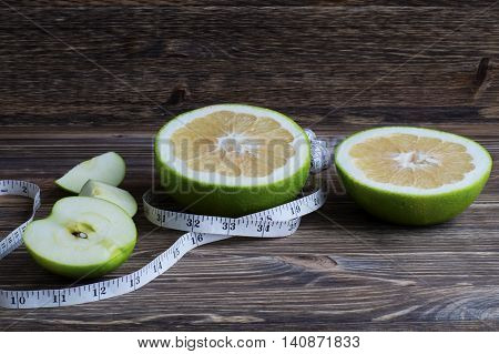Dieting concept. Closeup Pamela fruit and apples with measuring tape on table