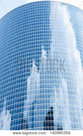 A skyscraper with reflections of clouds, sky and buildings.