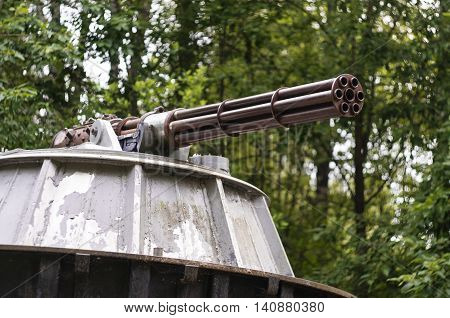 An old minigun on a stand in a forest.