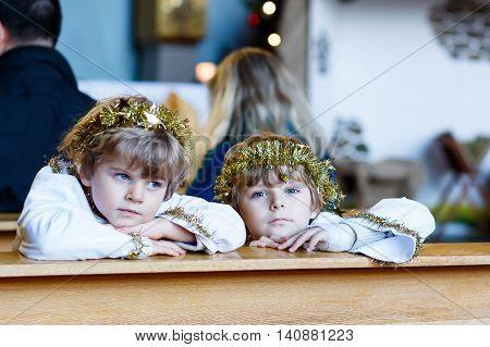 Two beautiful little kis in angel clothes for Christmas story in a church. Happy adorable blond children, boys singing and excited about holiday.