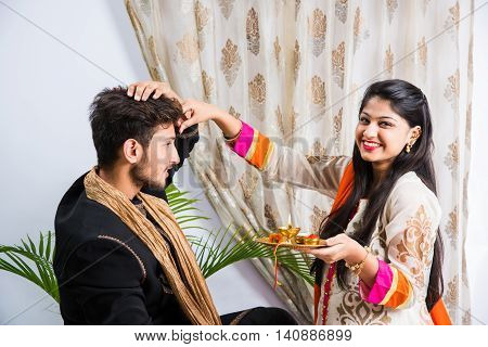 indian sister applying tika on brother's forehead, enjoying and celebrating Raksha Bandhan festival