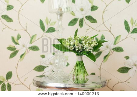 Small bouquet of Lily of the valley flowers standing on decorative metallic table with sea shells elements. Flower decor idea. Flower design. Interior