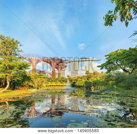 Singapore, Republic of Singapore - May 5, 2016: Gardens by the Bay with Supertree grove and Marina bay Sands hotel reflecting in lake at sunrise