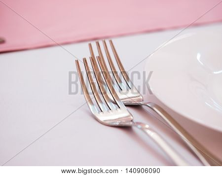 Two kitchen forks on dinner table with pink tablecloth