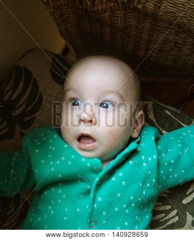 Open-eyed and surprised little baby boy in green clothe. Amazing and delighted face