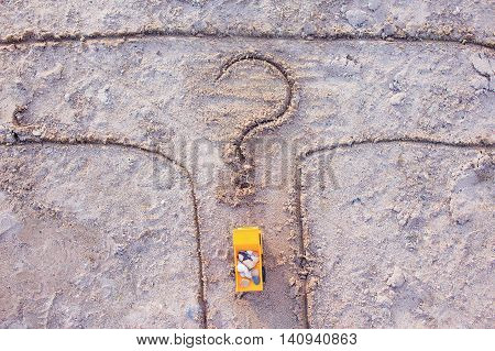 tipper with stones at crossroads. toy yellow truck on the sand at the fork in the road. drawn a question mark. the concept of honest business. top view