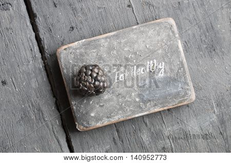 Eat heathy inscription and blackberries on a wooden table.