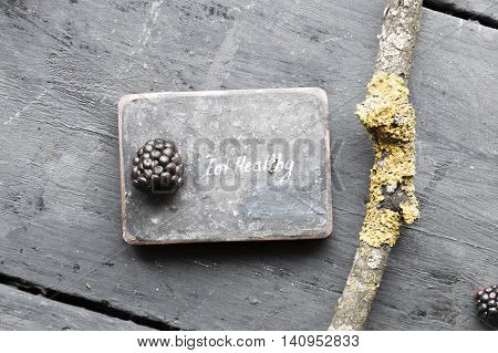 Eat heathy inscription and blackberries on a wooden table.