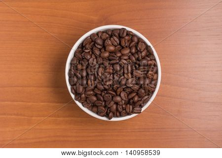 Coffee beans into a bowl over a wooden table. Coffea arabica