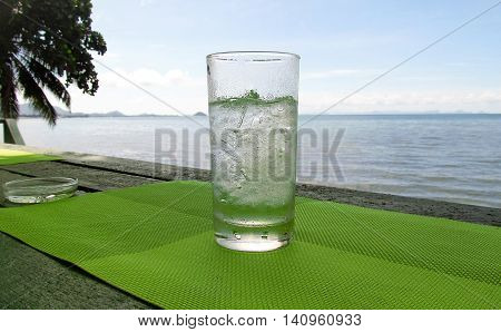 Glass of water with ice on background of the sea