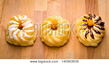 Three traditional French cruller chocolate plain vanilla on a wood surface