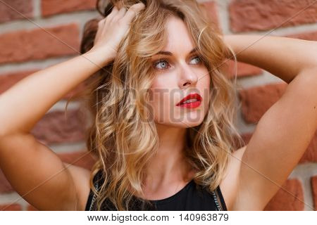 Beautiful blonde woman with natural make-up and gray eyes on brick background. Shoot on fast aperture