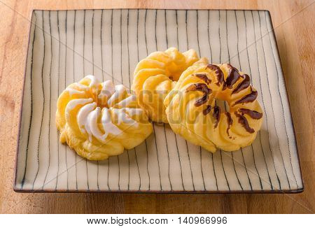 Three traditional French cruller chocolate plain vanilla on a bamboo pattern plate on wood surface
