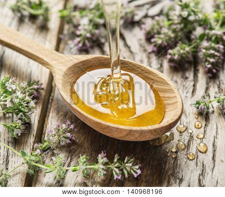 Herbal honey pouring into the wooden spoon. Spoon is on old wooden table surrounded with levender flowers. Honey drops.