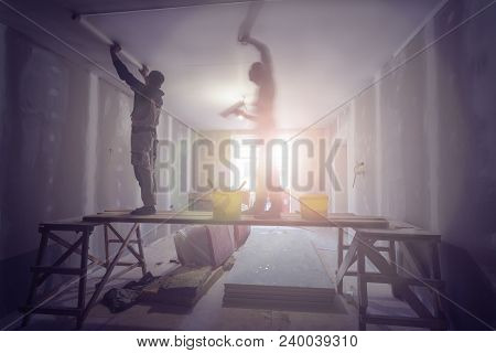 Two Workers Are Installing Ceiling From Wooden Scaffolding Platform In Apartment Is Under Constructi