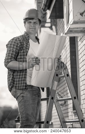 Black And White Portrait Of Constrcution Engineer Standing On Stepladder And Holding Blueprints