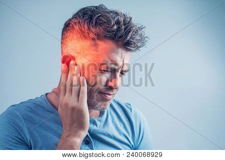 Male Having Ear Pain Touching His Painful Head Isolated On Gray Background