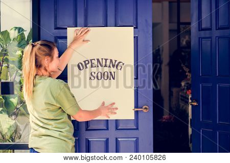 Woman putting on store opening soon sign