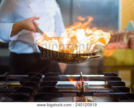 Chef cooking and doing flambe on food in restaurant kitchen