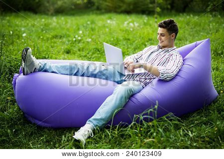 Handsome Young Man Lying On Inflatable Sofa Lamzac Sufring In Internet On Laptop While Resting On Gr