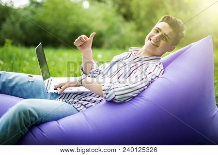 Handsome Young Smile Man Lying On Inflatable Sofa Lamzac Working On Laptop And Gesturing Thumbs Up W